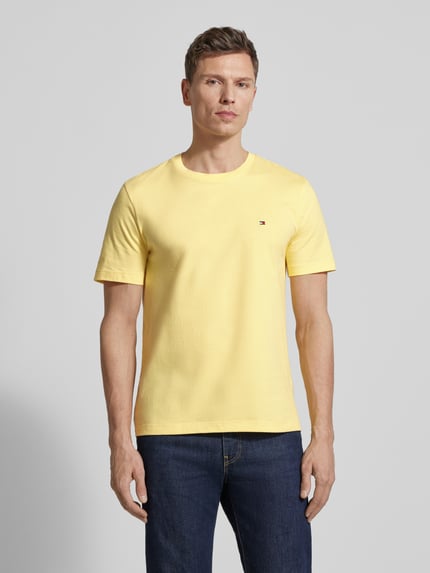 Männermodel trägt Regular Fit T-Shirt aus reiner Baumwolle von Tommy Hilfiger in Gelb, unifarben, Logo-Stitching, Jersey, Ganzkörperansicht von vorne.