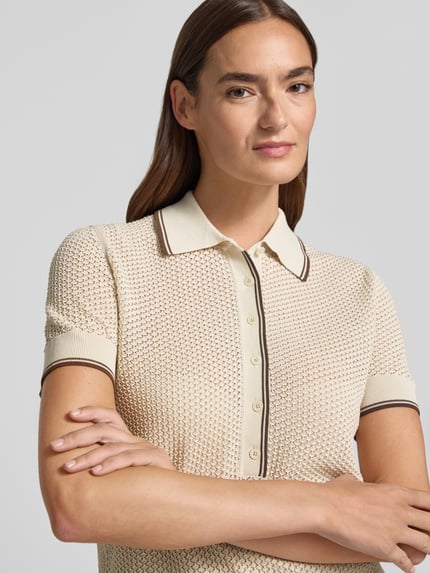 Modelka nosi Strickshirt mit Polokragen und Knopfleiste Modell 'MEROPE' od DRYKORN, czysta bawełna, krój regular fit, kremowy, zbliżenie na górną część ciała.
