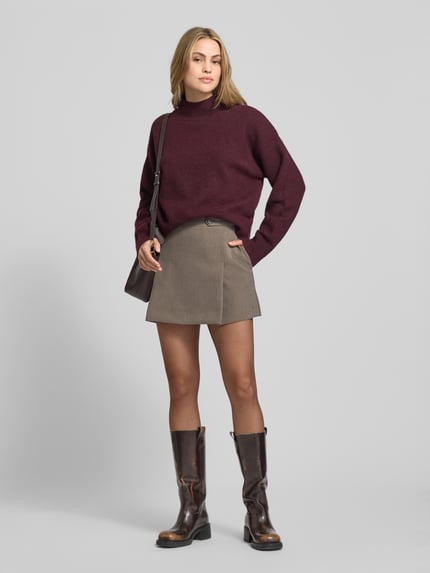 Vrouwenmodel draagt uitlopende mini-rok uit viscosemix van Tommy Hilfiger, unikleurig met logopatch, zijzakken, rits. Vooraanzicht hele lichaam.