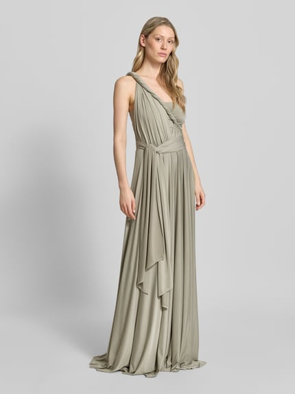 Vrouwenmodel draagt Maxikleid mit tiefem V-Ausschnitt van Rose Avenue, getailleerde fit, diepe V-hals, gekruiste bandjes achter, tailleband, lichte beige tint, vloeiende stofstructuur. Volledige lichaamsaanzicht van voren.