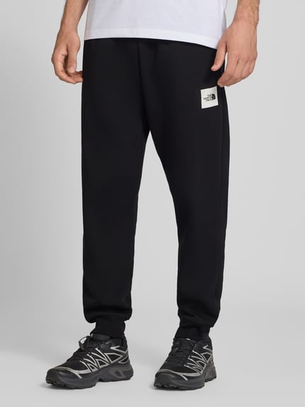 Männermodel trägt schwarze Regular Fit Sweatpants aus Escorial-Mix von The North Face mit Label-Print, Ganzkörperansicht von vorne.