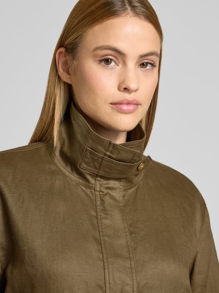 Kobieta nosi Relaxed Fit Utility-Jacke aus reinem Leinen od Tommy Hilfiger, efekt: jednolity kolor, stójka, aplikacja z logo, zapięcie kryty zamek błyskawiczny i listwa z zatrzaskami, długi rękaw z regulowanymi paskami, kieszenie z patką, materiał: len, zbliżenie na górną część ciała.