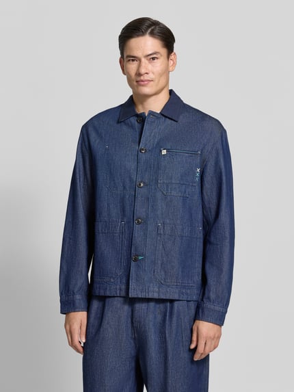 Männermodel trägt Regular Fit Hemdjacke in Denim-Optik von Scotch & Soda, reine Baumwolle, Kentkragen, Knopfleiste, aufgesetzte Taschen, Ganzkörperansicht von vorne.