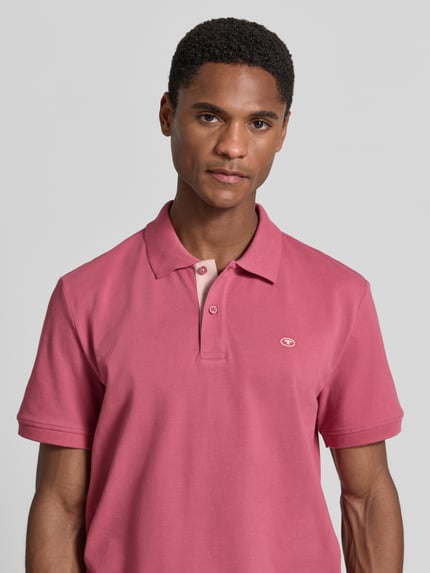 Männermodel trägt Regular Fit Poloshirt aus reiner Baumwolle von Tom Tailor in Rosa, glatte Textur, Nahaufnahme Oberkörper. Herren Poloshirt.