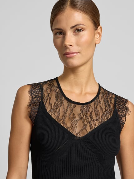 Frauenmodel trägt schwarzes Top mit Spitzenbesatz Modell 'LINGA' von YAS im Viskose-Mix, Ripp-Optik, Nahaufnahme Oberkörper.