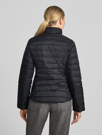 Frauenmodel trägt schwarze Slim Fit Steppjacke mit Logo-Detail von Lacoste, glatte Oberfläche, gesteppte Struktur, Ganzkörperansicht Rückansicht, Damen Steppjacke von Lacoste.