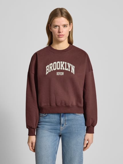Vrouwenmodel draagt Sweatshirt met Labelprint en ronde hals van Review in bruin, katoenmix, relaxed fit, labelprint, ronde hals, Ganzkörperaanzicht van voren.
