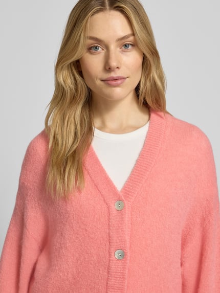 Frauenmodel trägt Strickjacke mit V-Ausschnitt Modell 'Petrinelle Hope' von MSCH Copenhagen in Rosa, Material-Mix mit Alpaka, Nahaufnahme Oberkörper.