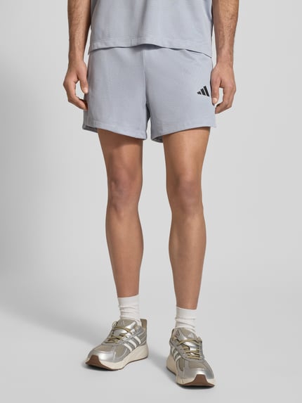 Männermodel trägt Shorts mit Label-Print von adidas Training, hellgrau, Lockerer-Schnitt, Elastischer-Bund, Ganzkörperansicht von vorne.