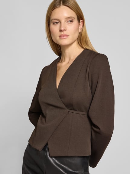 Kobiece modelka nosi żakiet z dekoltem w serek model 'Simmi' od Neo Noir z elastycznej mieszanki materiałów, taliowany krój, taśma do wiązania, kopertowy styl, długość tyłu w rozmiarze 36: 52 cm, szerokość w rozmiarze 36: 40 cm, długość rękawów w rozmiarze 36: 63 cm, widok z przodu, zbliżenie na górną część ciała