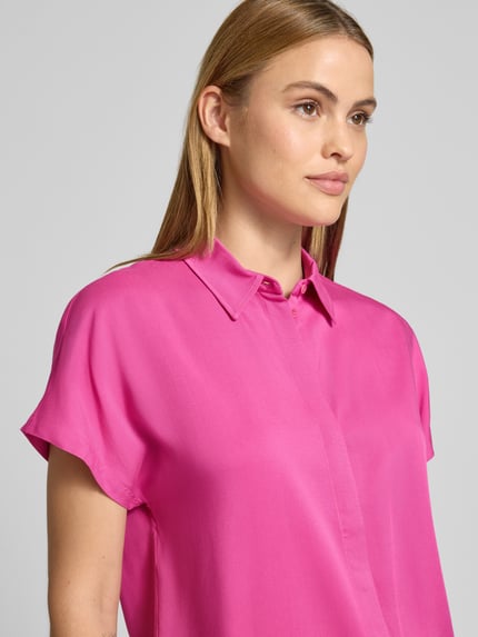 Modelka kobieca ma na sobie Relaxed Fit Hemdbluse aus reiner Viskose Modell 'LARISAANA' od Armedangels w jednolitym intensywnie różowym kolorze, krój relaxed fit, kołnierzyk koszulowy, dekolt w szpic, krótki rękaw, materiał popelina z czystej wiskozy; zbliżenie na górną część ciała z przodu.