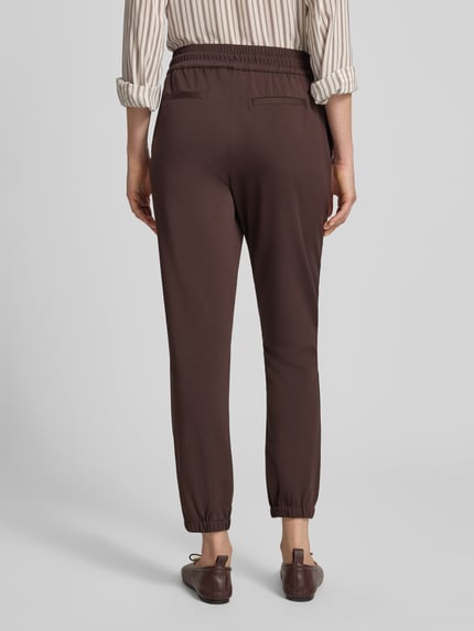 Frauenmodel trägt Jogger Pants mit Reißverschlusstasche Modell 'Jill' von monari in Braun, Straight Fit, elastischer Bund, Ganzkörperansicht Rückansicht.
