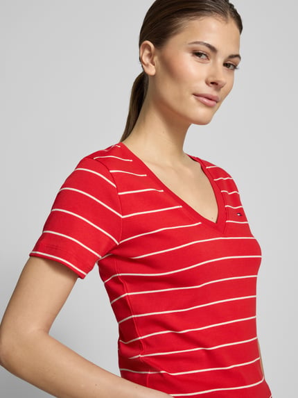Vrouwenmodel draagt 'Slim Fit T-shirt uit zuiver katoen' van Tommy Hilfiger in tweekleurige look, gestreept motief, rode jersey, logodetail, V-hals, korte mouw, detailopname bovenlichaam.
