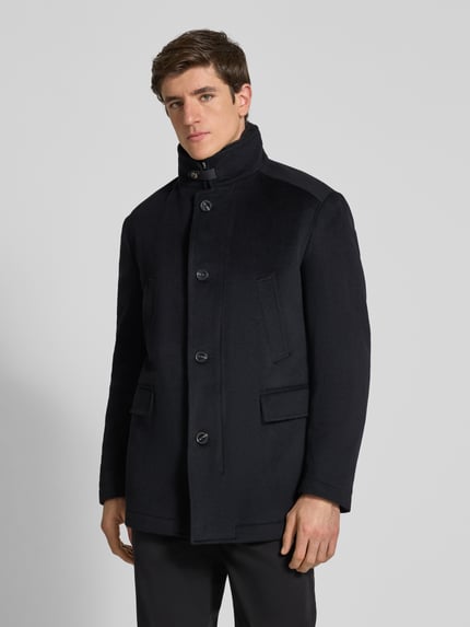 Männermodel trägt Mantel mit Stehkragen Modell '17 JO-48Gary' von JOOP!, dunkel, strukturiertes Gewebe, Taschen und Knöpfe, Ganzkörperansicht von vorne.