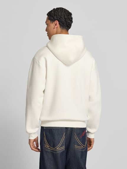 Męski model nosi Regular Fit Hoodie mit Känguru-Tasche od REVIEW z mieszanki bawełny, biały kolor, długość tyłu 70 cm, długość rękawów 62 cm, krój regular fit, kaptur, kieszeń kangurka, widok całej sylwetki z tyłu.