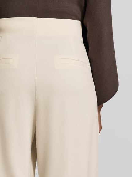 Frauenmodel trägt Relaxed Fit Anzughose mit Bundfalten Modell 'SC-SIHAM 103' von Soyaconcept in Creme, glatte Textur, Nahaufnahme Rückansicht, Damen Anzughose von Soyaconcept.