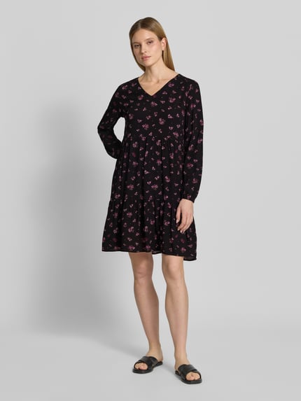 Vrouwenmodel draagt Minikleid aus Viskose mit V-Ausschnitt van Zero, zwarte stof met roze bloemen, getailleerd model, V-hals, elastische mouwboorden, ruglengte maat 36: 80 cm, borstwijdte 39 cm, mouwlengte 60 cm. Volledige lichaamsvoorzijde.