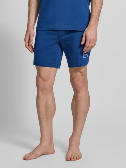 Männermodel trägt Regular Fit Sweatshorts aus Baumwoll-Mix Modell 'LAZE SHORTS CW' von HUGO, Optik: Unifarben, Label-Print, Bundabschluss: Elastisch; Nahaufnahme Unterkörper.