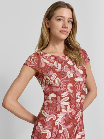 Vrouwenmodel draagt knielang 'Knielanges Cocktailkleid mit Applikationen' van Christian Berg Cocktail, materiaalmix met stretch, nauwsluitend model, ronde hals, florale applicaties in roze en crèmetinten, ruglengte maat 36: 89 cm, borstwijdte: 45 cm, mouwlengte: 11 cm, detailopname bovenlichaam.