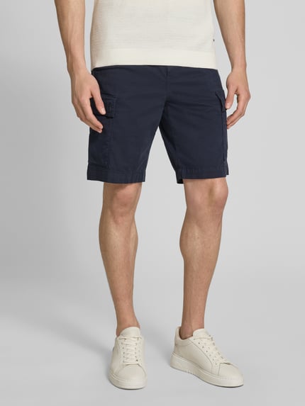 Männermodel trägt Relaxed Fit Cargoshorts aus Baumwoll-Mix Modell 'SISLA' von BOSS Orange in Dunkelblau, unifarben, mit Label Patch, Knopfverschluss und mehreren Taschen, Baumwollstruktur, Ganzkörperansicht von vorne.