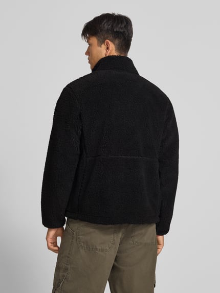 Männermodel trägt Fleecejacke mit Stehkragen und Brusttasche Modell 'EXTREME PILE' von The North Face aus schwarzem Teddyfell, Rückenansicht. Die Jacke hat Regular Fit, Reißverschluss, Label-Stitching, Rückenlänge 67 cm, Ärmellänge 70 cm.
