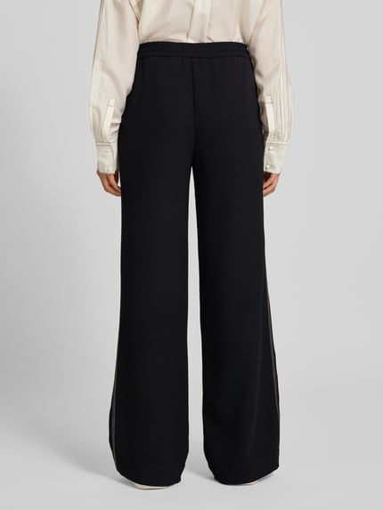 Vrouwenmodel draagt Hose mit weitem Bein und Eingrifftaschen van Marc Cain in zwart met galonstrepen, elastische band, persplooien, steekzakken, bandwijdte maat 36: 39 cm, binnenbeenlengte maat 36: 83 cm, volledig van achteren gefotografeerd.