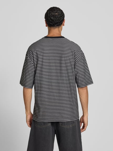 Männermodel trägt Herren T-Shirt mit feinen schwarzen und grauen Streifen, Produktname T-Shirt mit Logo-Stitching Modell 'Dupree' von Carhartt Work In Progress, Reine Baumwolle, Boxy-Fit, Rundhalsausschnitt, Rückenlänge bei Größe M 70 cm, Ganzkörperansicht Rückansicht.