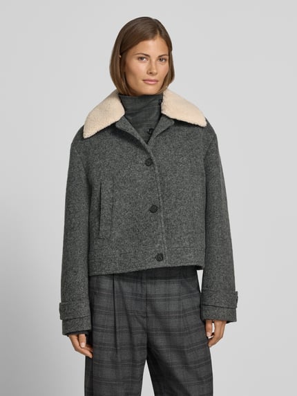 Frauenmodel trägt Jacke mit Kentkragen und Eingrifftaschen von Style Icon Collection in Grau, sichtbare Knopfleiste, Ganzkörperansicht von vorne. Gerader Schnitt, seitliche Eingrifftaschen, Ärmelriegel mit Knopf, Struktur aus weichem Wollstoff, dezente Karomuster-Hose, Kontext: Rückenlänge 54 cm, Schulterbreite 52 cm, Brustweite 50 cm, Ärmellänge 60 cm.