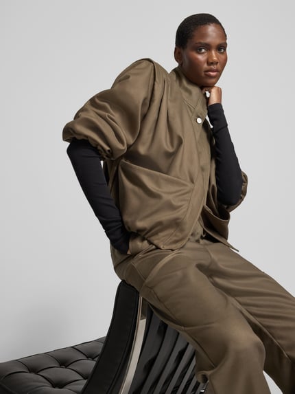 Frauenmodel trägt Funktionsjacke mit großen Fronttaschen von black palms in unifarbener Optik, strukturierte Webware, Loose Fit, Ziertaschen, aufgesetzte Seitentaschen, lange Ärmel, Stehkragen, Druckknöpfe, elastische Abschlüsse, Ganzkörperansicht von vorne.