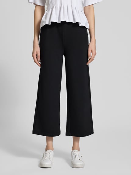 Vrouwenmodel draagt Wide Fit Sweatpants in verkorte pasvorm model 'Banu' van Soyaconcept, elastische materiaalmix met modal, wide fit, tunnelkoordband, zwart, glad oppervlak, dames sweatpants, verkort, vooraanzicht, detailopname onderlichaam.