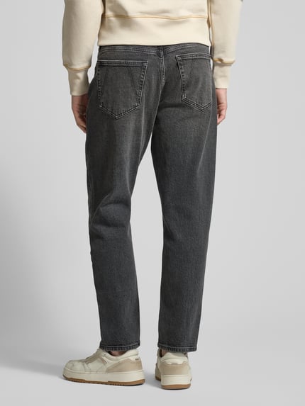 Männermodel trägt Tapered-Fit Herren Jeans aus Bio-Baumwoll-Mix Modell 'MAAKX' von Armedangels in dunkler Denim-Optik, Ganzkörperansicht Rückansicht. Passform: Relaxed Tapered-Fit, Mid Waist, Label-Patch, Gürtelschlaufen, 5-Pocket-Design, Verschluss: Knopf und Reißverschluss.