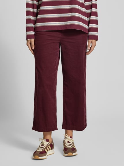 Modelka kobieca nosi Loose Fit Cordhose aus reiner Baumwolle od Marc O'Polo DENIM, bordowe, szerokie nogawki, tekstura sztruksu, widok całej sylwetki od przodu.