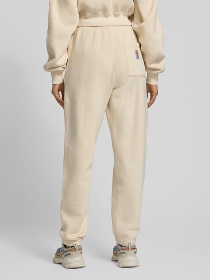 Frauenmodel trägt Sweatpants mit elastischem Bund Modell 'FIKY' von American Vintage aus Baumwoll-Elasthan-Mix, Regular-Fit, cremefarben, Damenmode, sichtbarer Tunnelzug und Gesäßtasche, ganzkörperansicht Rückansicht.