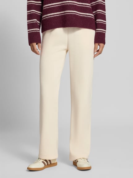 Kobieta nosi Wide Fit Sweatpants aus Baumwoll-Mix Modell 'Iconic' od Gina Tricot, kremowy kolor, elastyczny pas, widok z przodu, spodnie damskie z bawełny z domieszką, szeroki krój, długość nogawki 80 cm w rozmiarze S.