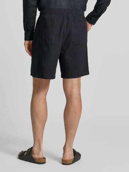 Männermodel trägt Leinenshorts mit elastischem Bund von GAP in Schwarz, Loose-Fit, Gesäßtaschen, Leinen-Baumwoll-Anteil, Ganzkörperansicht Rückansicht.