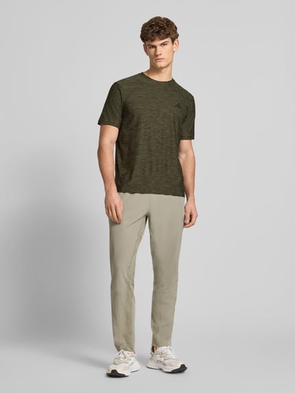 Männermodel trägt T-Shirt mit Label-Print von adidas Training in Olivgrün, Regular Fit, Material-Mix mit Stretch, Ganzkörperansicht von vorne.