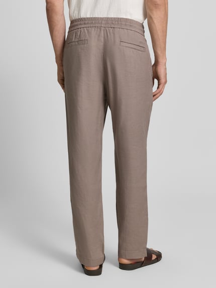 Männermodel trägt Straight Fit Schmale Hose aus Leinen-Lyocell-Mix Modell 'CINO' von HUGO in Taupe, elastischer Bund, Rückansicht Ganzkörperansicht.