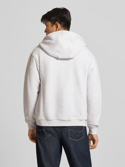 Männermodel trägt Relaxed Fit Sweatjacke aus Baumwoll-Mix Modell 'ORSALAMANCO' von JACK & JONES in Hellgrau mit Kapuze, Ganzkörperansicht Rückansicht.