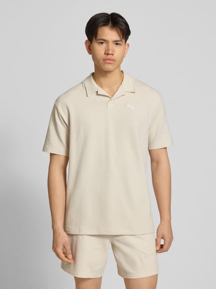 Männermodel trägt Regular Fit T-Shirt mit Logo-Stitching von PUMA PERFORMANCE, beige, Strukturmuster, Reverskragen, Nahaufnahme Oberkörper.
