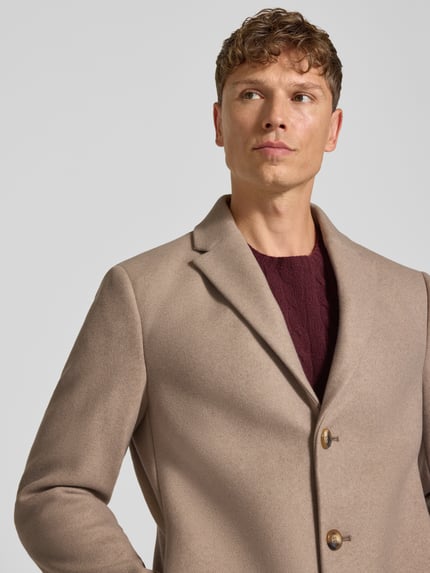 Mannenmodel draagt Relaxed Fit Mantel aus reiner Baumwolle Modell ‘AMSTERDAM‘ van MCNEAL in beige met reverskraag, knopen, katoenen textuur, Nahaufnahme bovenlichaam. Ruglengte 99 cm, schouderbreedte 46 cm, borstwijdte 52 cm, mouwlengte 66 cm.