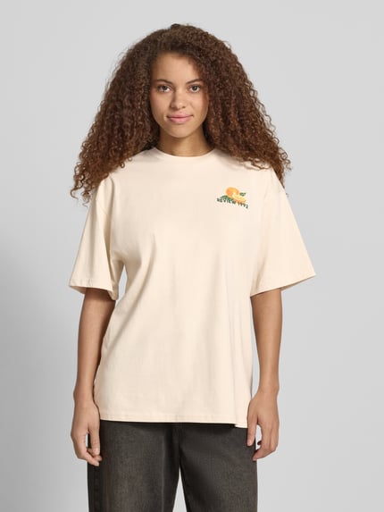 Vrouwenmodel draagt T-shirt met rückseitigem motiefprint van REVIEW in oversized fit van puur katoen, ronde hals, ruglengte maat S 68 cm, geheellichaamsaanzicht van voren.