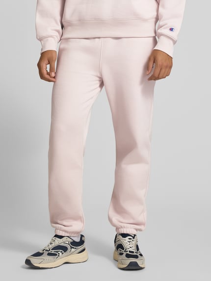 Mężczyznamodel nosi spodnie dresowe 'Sweatpants mit Label-Detail' od Champion, mieszanka bawełny, prosty krój, elastyczny pas z tunelem, wpuszczane kieszenie, detal z logo, długość wewnętrzna nogawki w rozmiarze M: 75 cm, widok całej sylwetki z przodu.