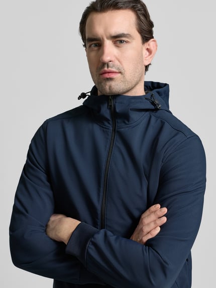 Männermodel trägt Regular Fit Funktionsjacke mit Kapuze von Tom Tailor Denim in Dunkelblau, unifarben, Nahaufnahme Oberkörper. Jacke ist wasserdicht, atmungsaktiv und wärmeisoliert, mit Stehkragen, Tunnelzug und Reißverschluss.