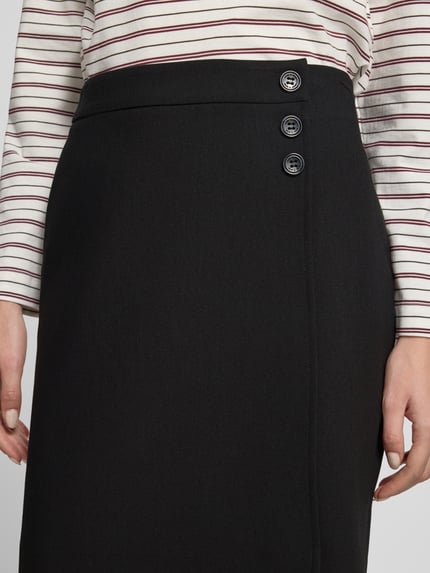Frauenmodel trägt Minirock mit Viskose-Anteil von MORE, schwarzer Stoff, glatte Textur, sichtbare Knöpfe, Nahaufnahme Oberkörper.