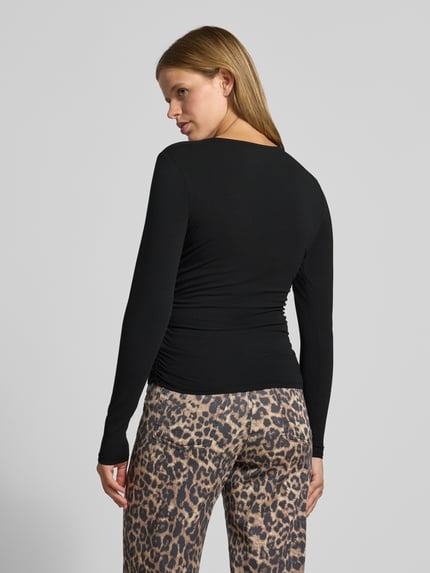 Frauenmodel trägt schwarzes Regular Fit Langarmshirt aus Baumwoll-Mix Modell 'MIRA' von ONLY, kombiniert mit gemusterten Hosen, Ganzkörperansicht Rückansicht. Damen Langarmshirt von ONLY.