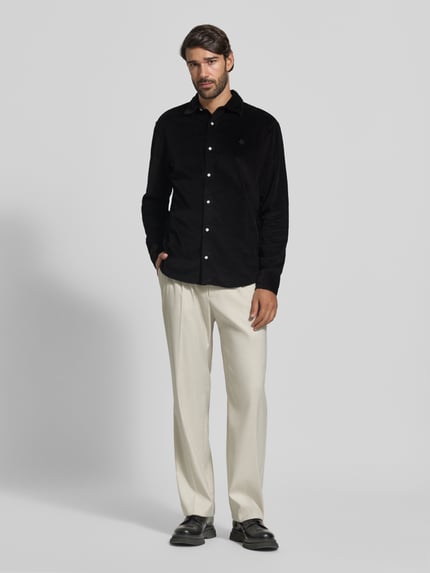 Männermodel trägt Regular Fit Freizeithemd mit Label-Stitching von MCNEAL aus schwarzem Cord mit Kentkragen, Ganzkörperansicht von vorne.