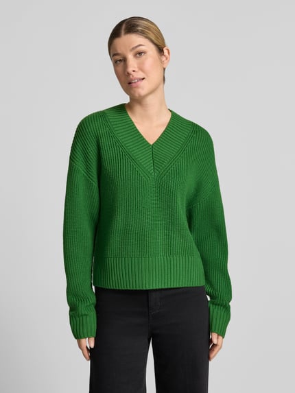 Modelka nosi sweter z dzianiny z czystej żywej wełny z dekoltem w serek 'Strickpullover aus Schurwolle mit V-Ausschnitt' od windsor., gruby ścieg, krój relaxed fit, intensywnie zielony kolor, długość tyłu 54 cm, długość rękawów 58 cm, widok całej sylwetki z przodu.