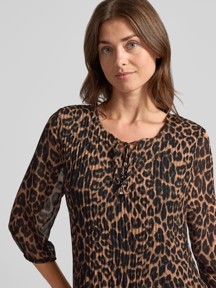 Modelka kobieca nosi Knielanges Kleid mit Schlüssellochausschnitt von ZABAIONE, wzór w cętki, krój relaxed fit, długość do kolan, efekt plisowania, rękaw o dł. 1/2, Długość tyłu w rozmiarze S: 93 cm, Szerokość w rozmiarze S: 47 cm, Długość rękawów w rozmiarze S: 44 cm, ujęcie: zbliżenie górnej części ciała.