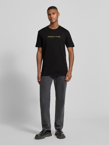 Männermodel trägt T-Shirt mit Label-Print von Armani Exchange, schwarze Reine Baumwolle, Regular-Fit, Rundhalsausschnitt, Ganzkörperansicht von vorne. Rückenlänge bei Größe M: 71 cm.