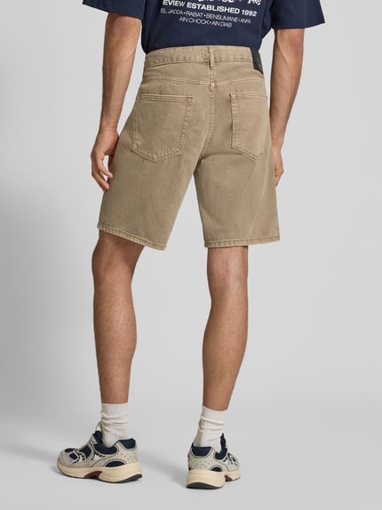 Männermodel trägt Regular Fit Jeansshorts aus reiner Baumwolle Modell 'EDGE' von Only & Sons in Denim-Optik mit Nieten, Label-Patch, 5-Pocket-Design; Farbe Beige, Materialstruktur glatt, Ganzkörperansicht Rückansicht.